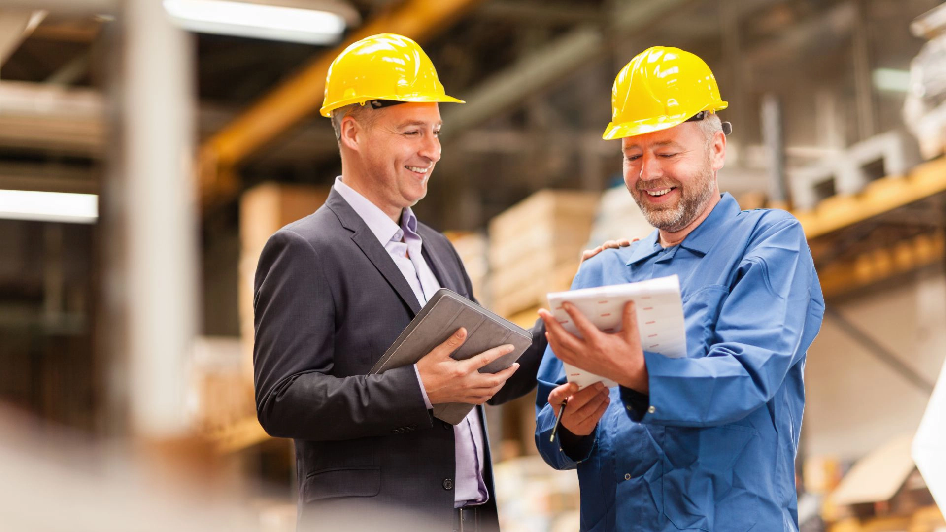 Two workers in hard hats talking in a warehouse